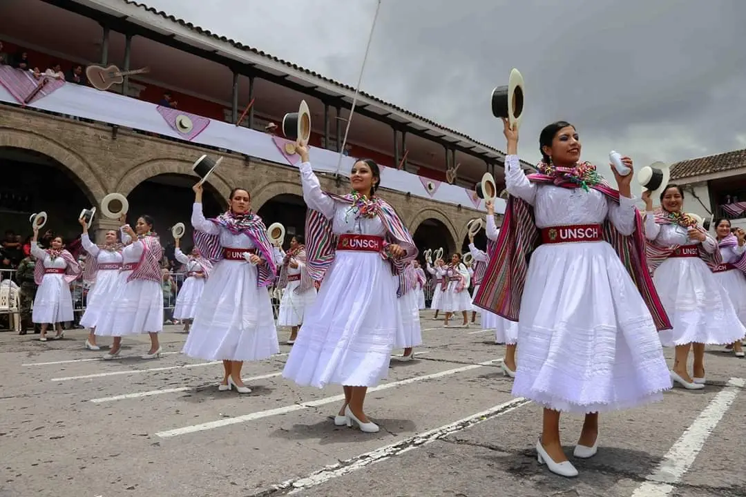 Danzantes con faldas blancas y mantas de colores levantan sus sombreros en una plaza de Ayacucho.