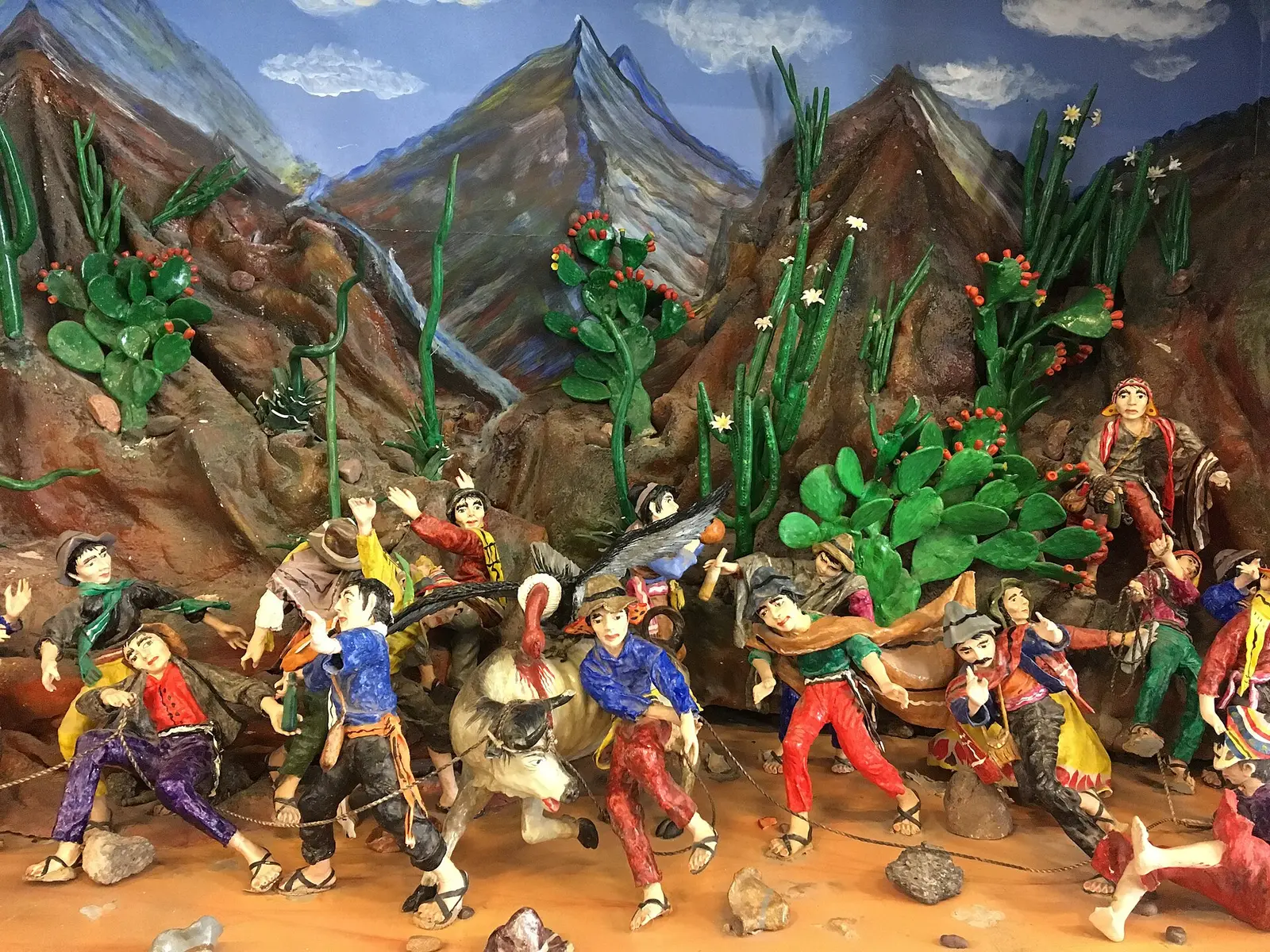 Detalle de un retablo ayacuchano: figuras de colores en fiesta frente a cerros y tunas.